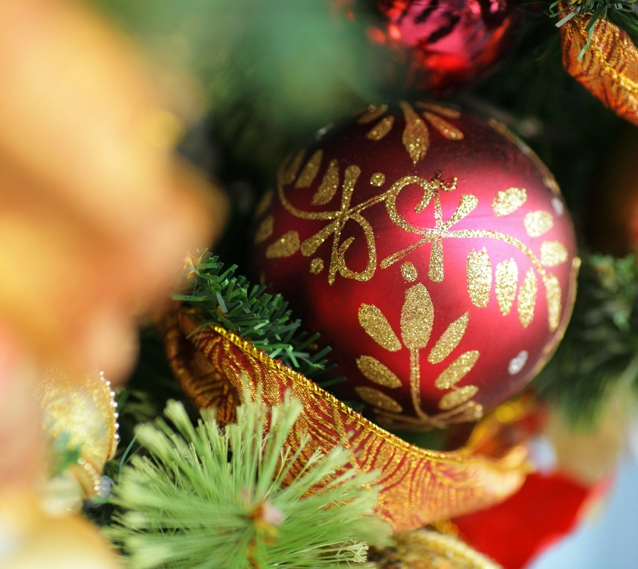 Czerwona bombka choinkowa z złotym wzorem, zawieszona na udekorowanym drzewku bożonarodzeniowym